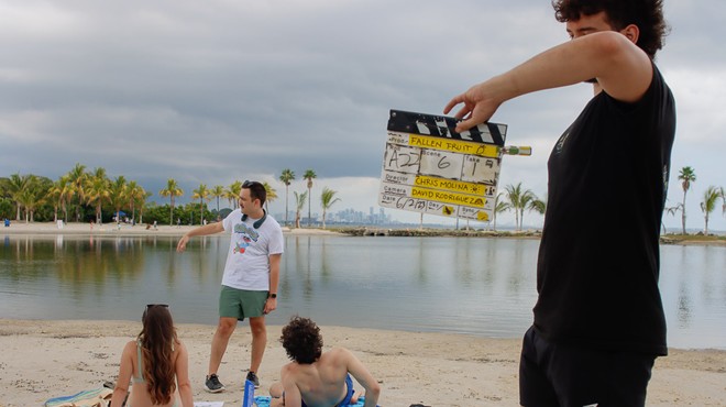Chris Molina is speaking with actors lying on the beach while a man holds a film slate in the foreground