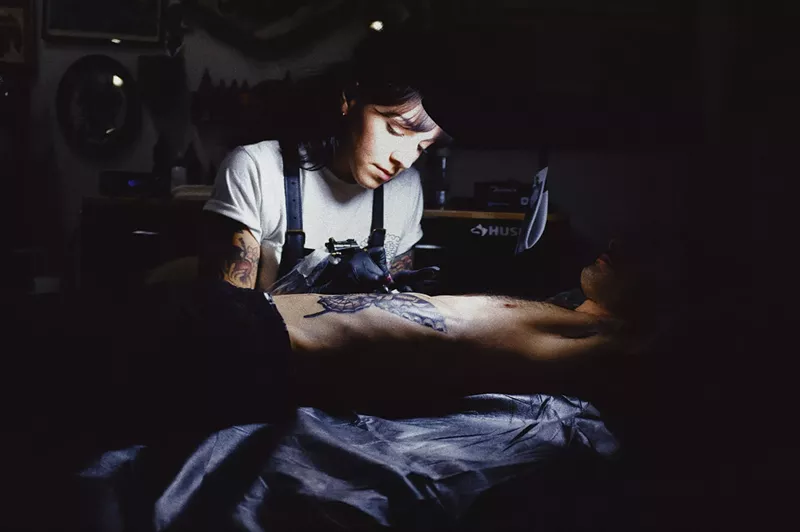 Image: A woman tattooing a client
