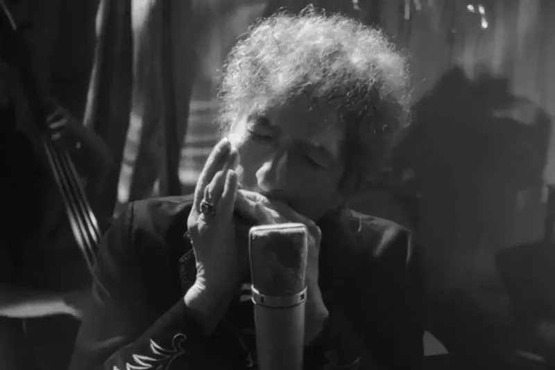 Image: Bob Dylan playing the harmonica in front of a microphone