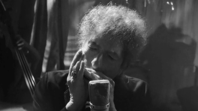 Bob Dylan playing the harmonica in front of a microphone