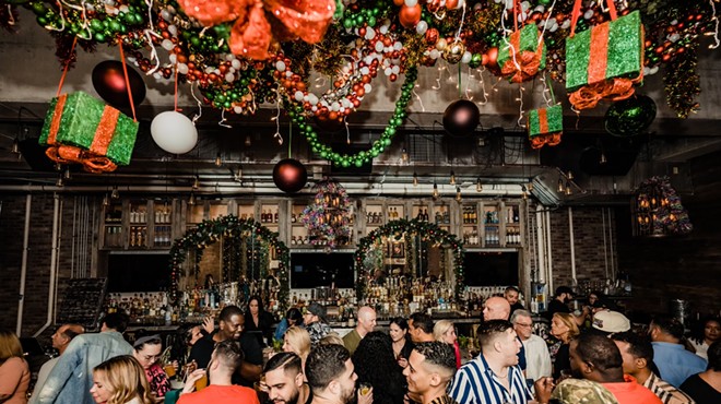 Guests mingle with cheer as they're surrounded by fun holiday decorations at Bodega Taqueria y Tequila. The ceiling is draped in holiday decoras guests hold and sip colorful holiday cocktails.