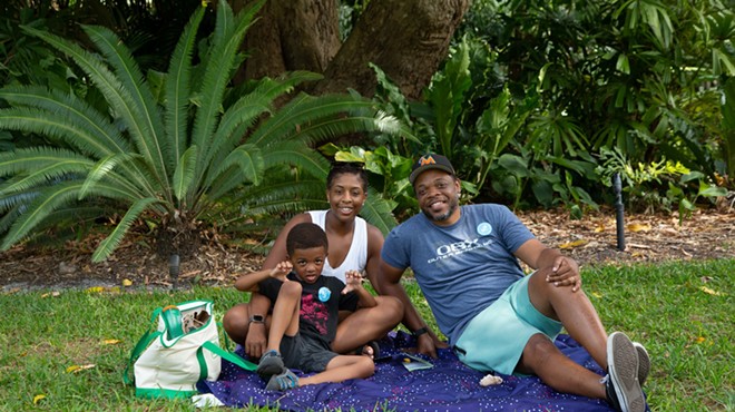 A mother and father with their child sitting on a picnic blanket at Fairchild Tropical Botanic Garden