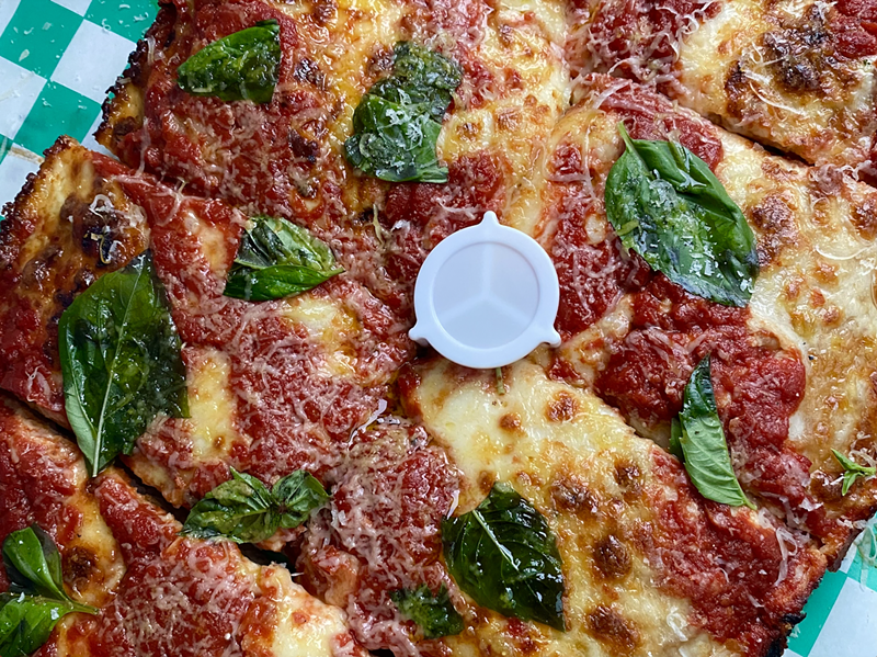 Image: A close-up photo of a pizza from Old Greg's Pizza covered in cheese and basil
