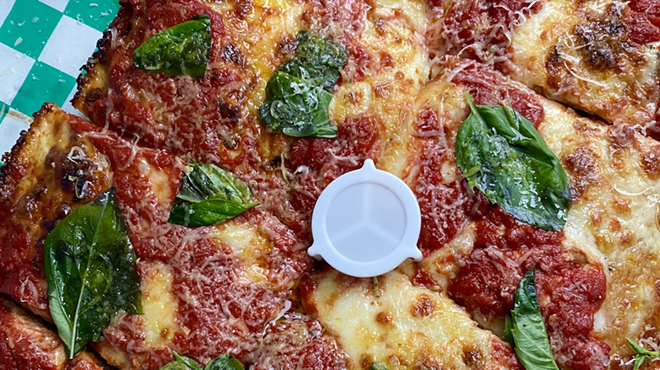 A close-up photo of a pizza from Old Greg's Pizza covered in cheese and basil