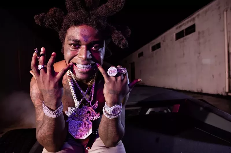Image: Closeup color photo of Kodak Black at night, showing off bling and grill