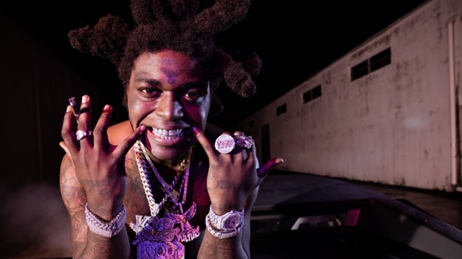 Closeup color photo of Kodak Black at night, showing off bling and grill