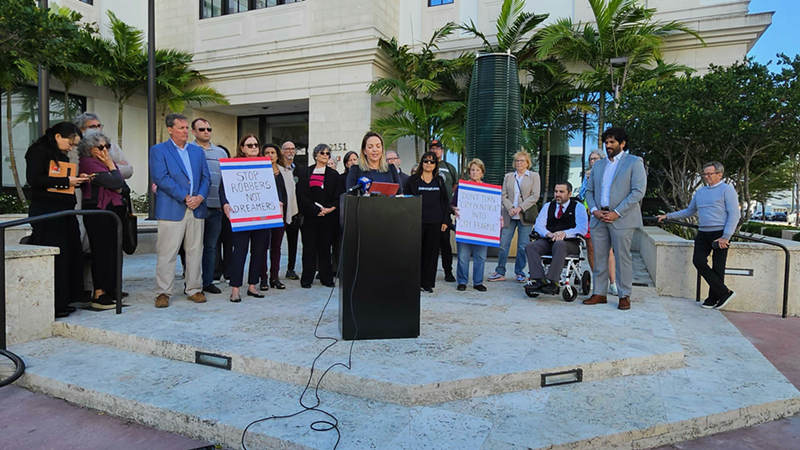 Image: Laura Kelley, Chair of the Miami-Dade Democratic Party, speaks at a press conference while people stand behind her