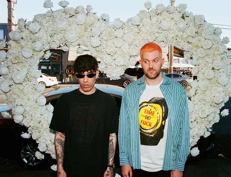 Image: Two musicians are posing in front of a heart made out of flowers.