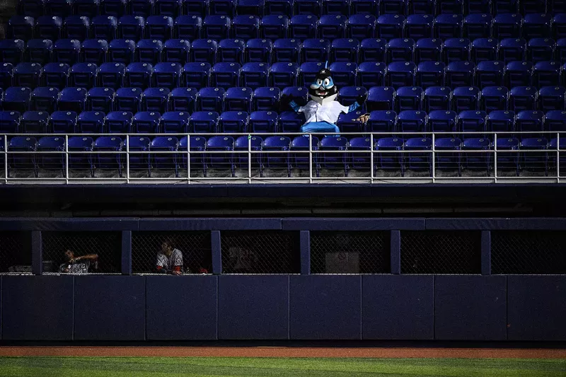 Image: 2020 photo of Miami Marlins mascot Billy the Marlin at a late-season game at Marlins Park, sprawled in a dark blue seat in an otherwise-empty section overlooking the left field bullpen