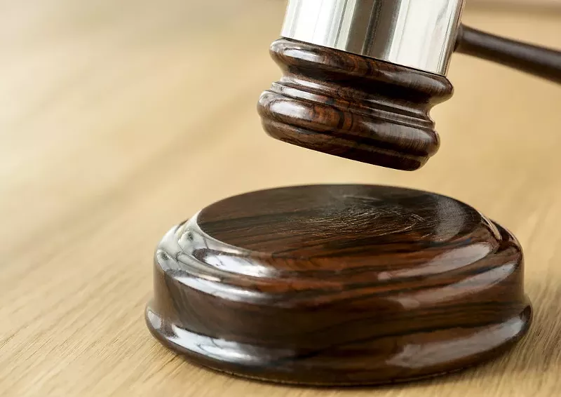 Image: A judge's gavel hangs above a wooden surface.