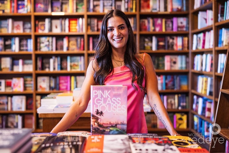 Author Asha Elias stands with her debut novel, Pink Glass Houses.