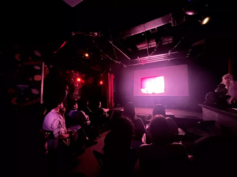Image: A group of people sitting in a dark room watching a film projection