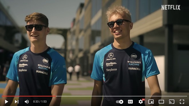 Williams Racing Formula 1 drivers Logan Sargeant (left) and Alex Albon (right) walk alongside each other wearing sunglasses.