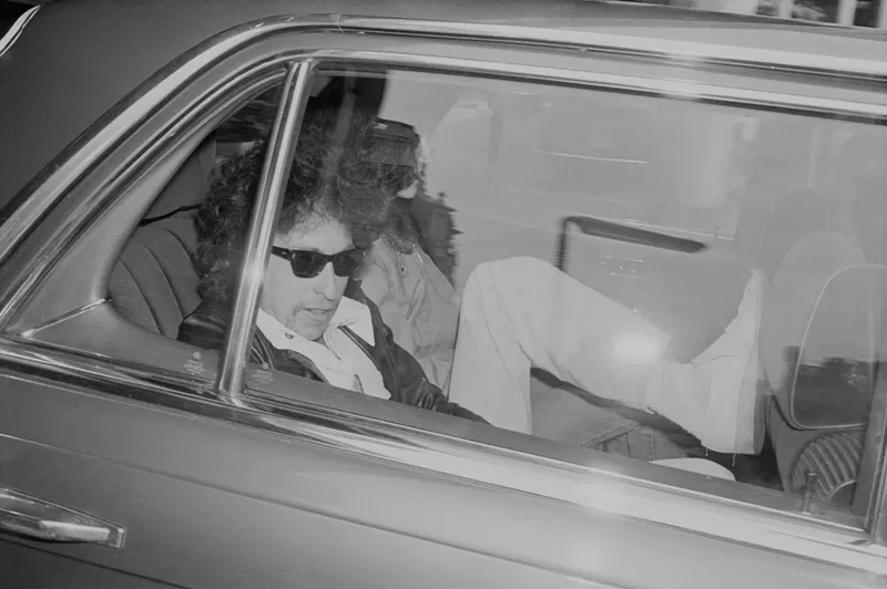 Image: Black and white image of Bob Dylan in the back of car