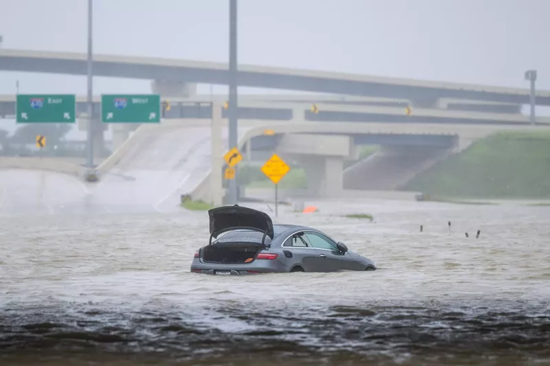 Image: A vehicle with its trunk open in the middle of deep floodwaters on a highway