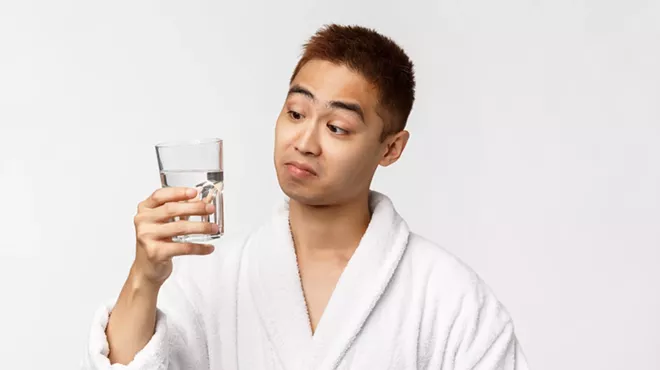 Portrait of Asian man in bathrobe looking skeptical while holding glass of water
