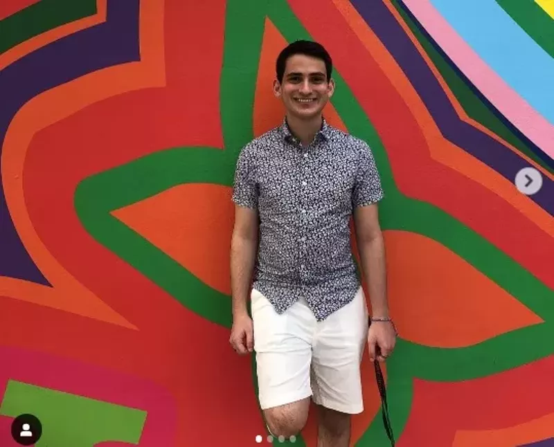 Image: A smiling university student is standing against a colorful abstract art background