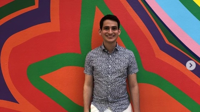 A smiling university student is standing against a colorful abstract art background