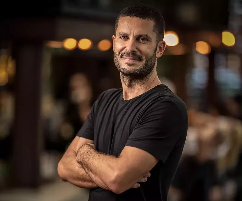 Image: A headshot of Miami restaurateur Coco Coig wearing a black shirt taken at a restaurant.