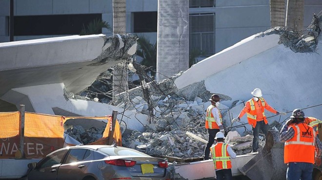 Construction workers in bright orange vests examine the debris-ridden site of the fatal Florida International University (FIU) bridge collapse. A gray Kia appears to be crushed beneath a large slab of concrete and mangled cables.