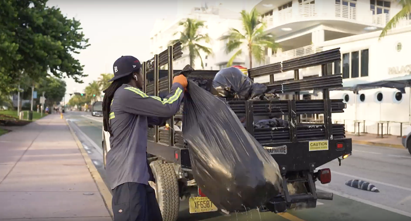 Image: A South Florida garbage collection worker tosses trash into a truck's flatbed