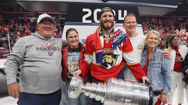 Panthers player Matthew Tkachuk holds the Stanley Cup trophy as his family stands shoulder to shoulder next to him, smiling