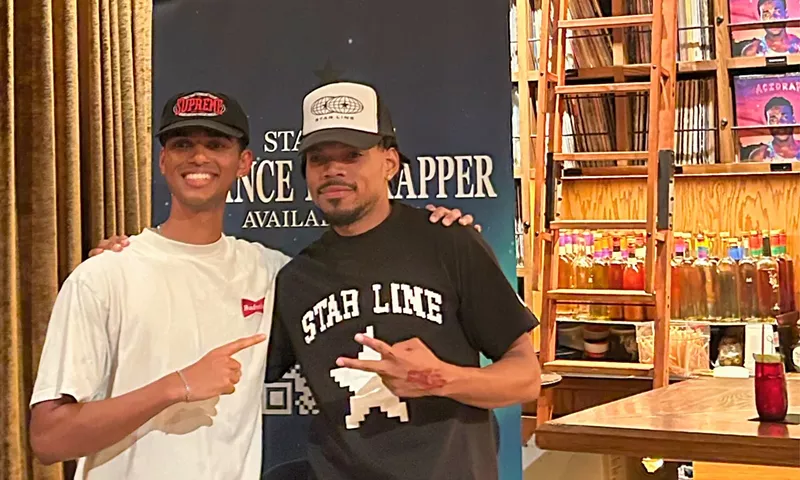 Image: Picture of Chance the Rapper posing with a fan next to a banner.