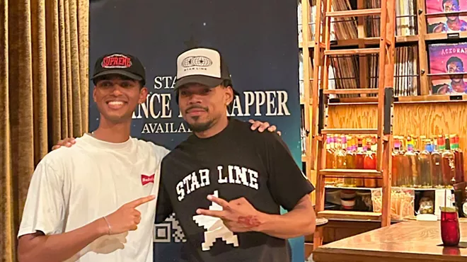 Picture of Chance the Rapper posing with a fan next to a banner.