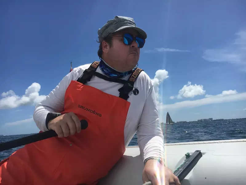 Image: Portrait of man at sea with a sailboat in the background