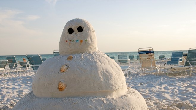 A snowman made of sand sits on a sunny beach.