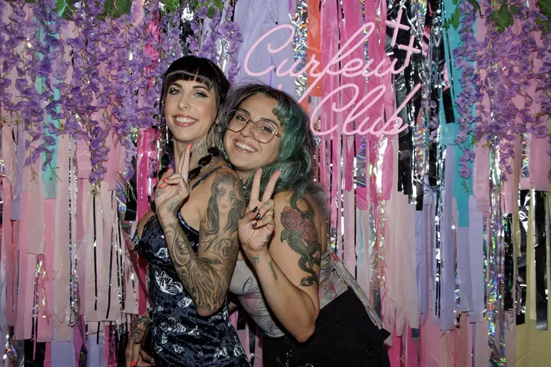 Image: Two women pose in front of a Curfew Club backdrop