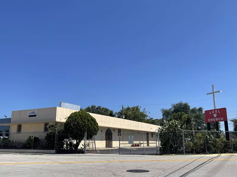 Image: A tan building sits at the corner of SW 13th Street and SW 4th Avenue.