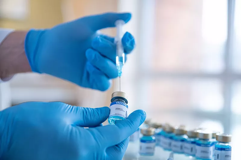 Image: stock photo showing a the hands of a gloved lab worker filling a syringe from an ampule with more ampules in the blurred background