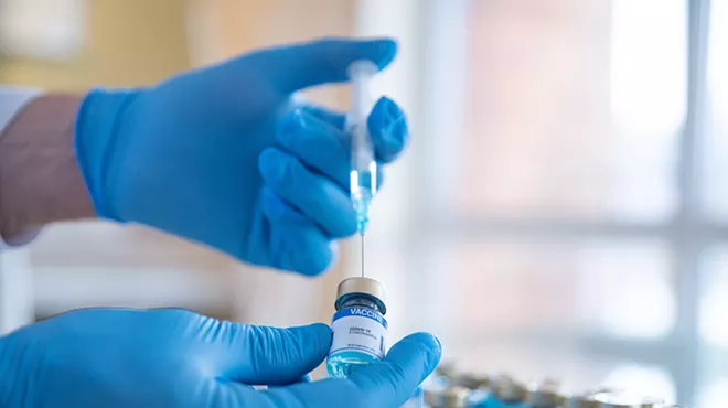 stock photo showing a the hands of a gloved lab worker filling a syringe from an ampule with more ampules in the blurred background