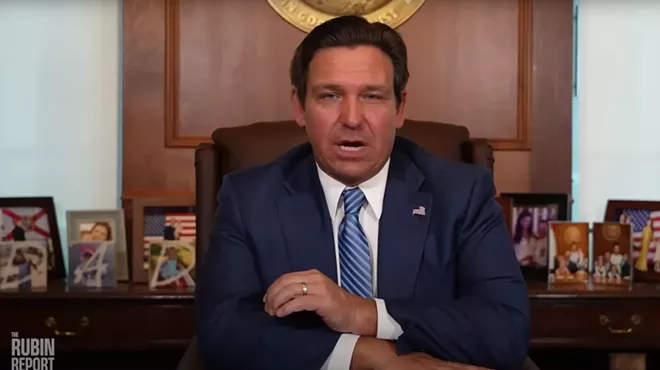 Ron DeSantis wearing a blue tie sitting at his desk