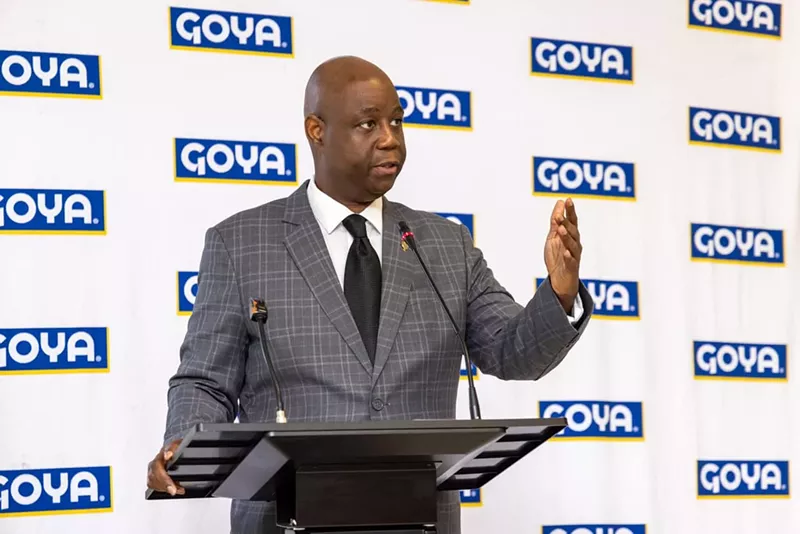 Image: photo of a Black man at a podium with Goya Foods logos behind him