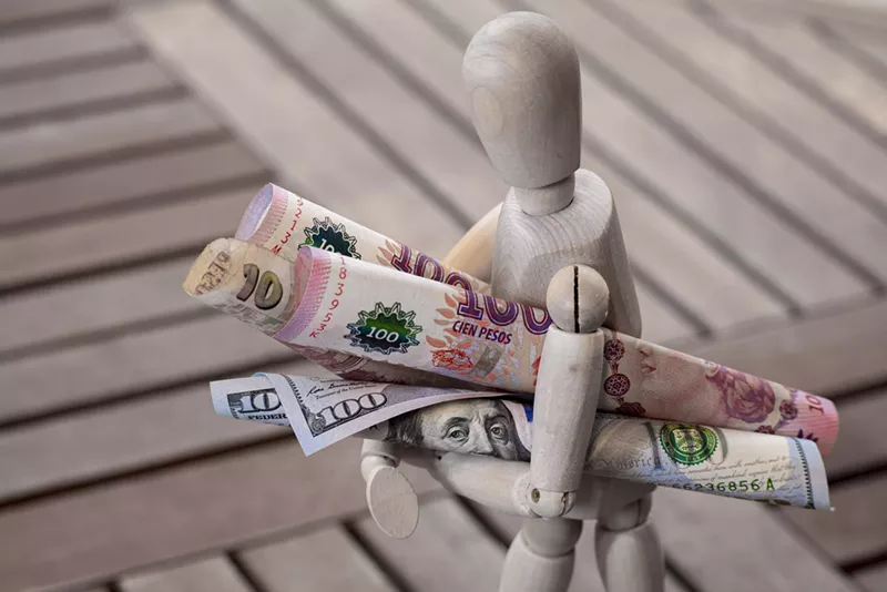 Image: A stock photo of a faceless figurine carrying Argentinian pesos and U.S. dollars