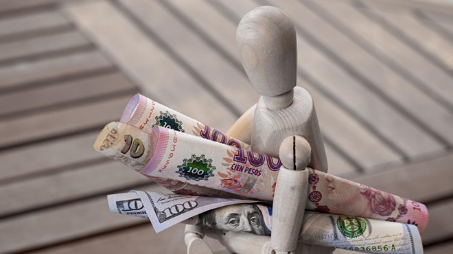 A stock photo of a faceless figurine carrying Argentinian pesos and U.S. dollars