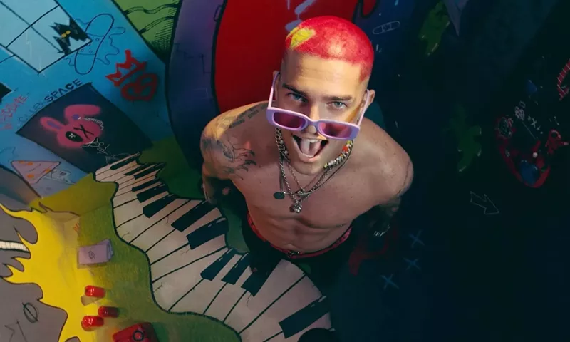 Image: Picture of a man with red hair and tattoos standing in front of a mural.