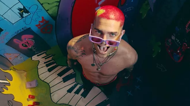 Picture of a man with red hair and tattoos standing in front of a mural.