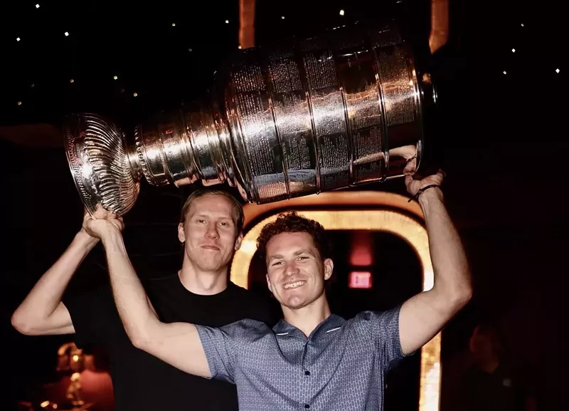 Image: two members of the NHL's Florida Panthers hoisting the 2025 Stanley Cup trophy inside a restaurant