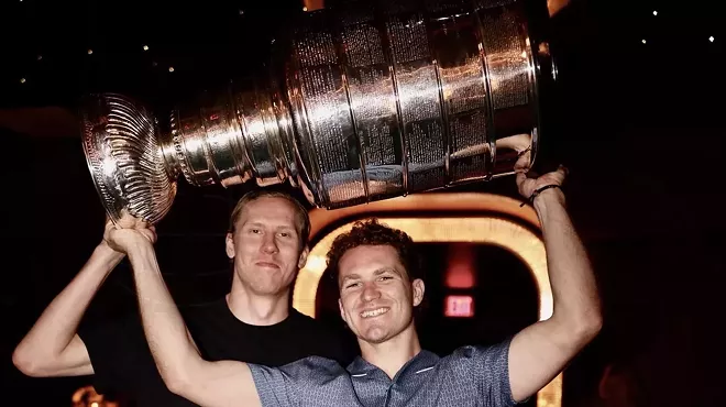 two members of the NHL's Florida Panthers hoisting the 2025 Stanley Cup trophy inside a restaurant