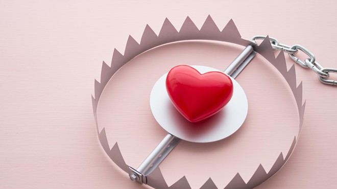 A bright red heart is surrounded by sharp, metal circular trap connected to a chain
