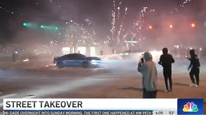 A car spins around an intersection during a street takeover as fireworks explode in the background
