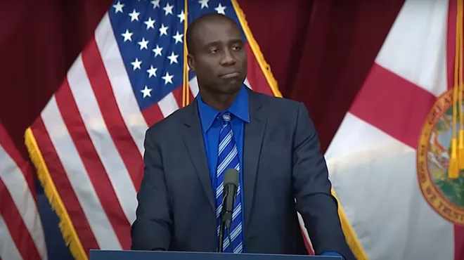 Florida Surgeon General speaking at press conference wearing a blue tie and black jacket