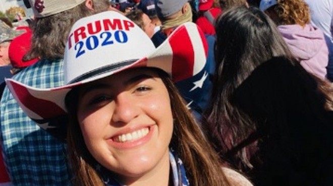 color photo of a smiling young woman wearing a white, red, and blue Trump 2020 hat