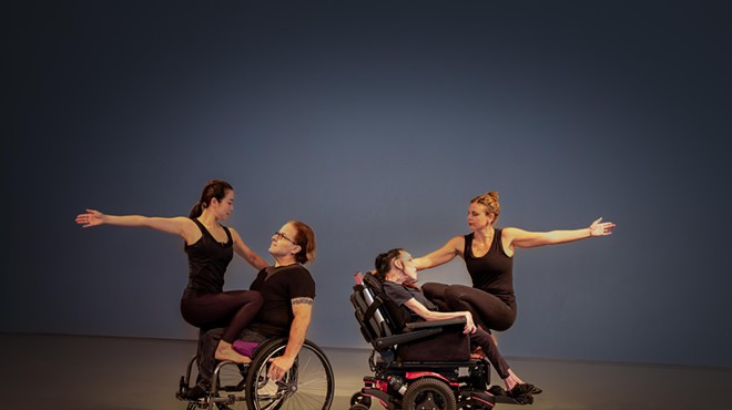 color photo of two sets of partners performing a dance on a stage; each partnership consists of one dancer who uses a wheelchair and one who does not