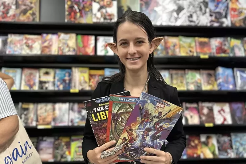 Image: A woman with prosthetic ears holding comic books in her hands