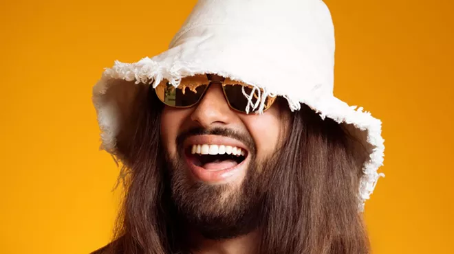 Picture of a man with long hair wearing a white hat against a yellow background.