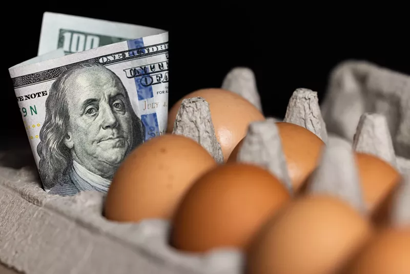 Image: color stock photo of a cardboard carton of brown eggs with a $100 bill tucked into one slot